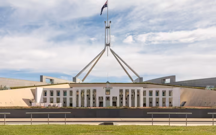 Wide exterior view of Parliament House, Canberra, with a flagpole against a cloudy sky
