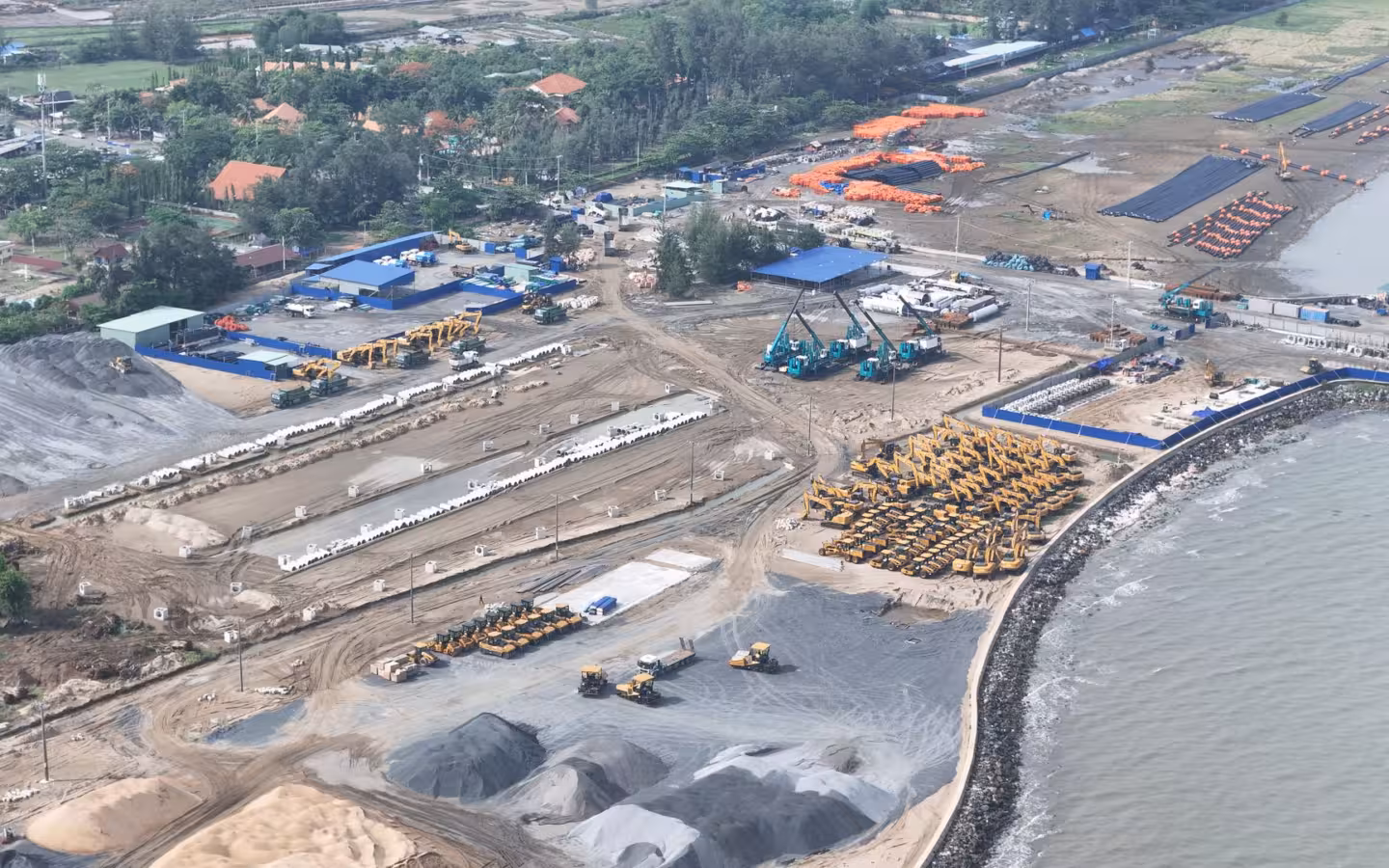 Aerial view of a construction site near water with machinery and buildings