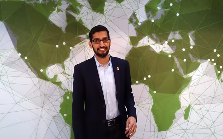 Sundar Pichai standing before a green world map backdrop