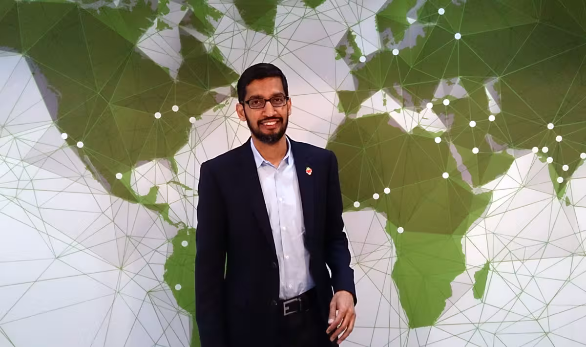 Sundar Pichai standing before a green world map backdrop