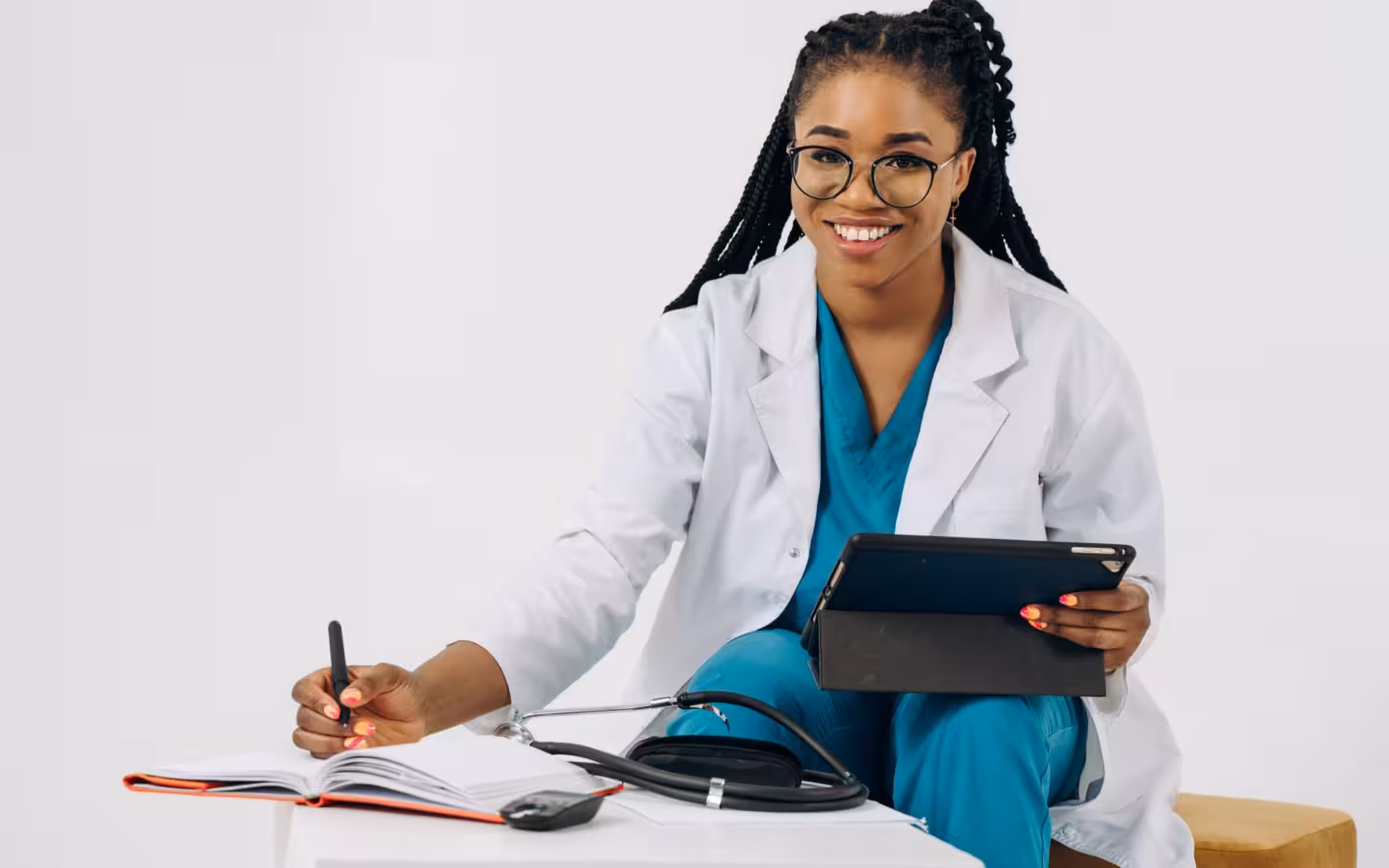 a smiling female doctor in scrubs holding a tablet and writing notes