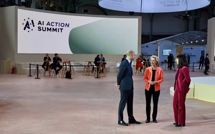 Three people standing in front of AI Action Summit screen