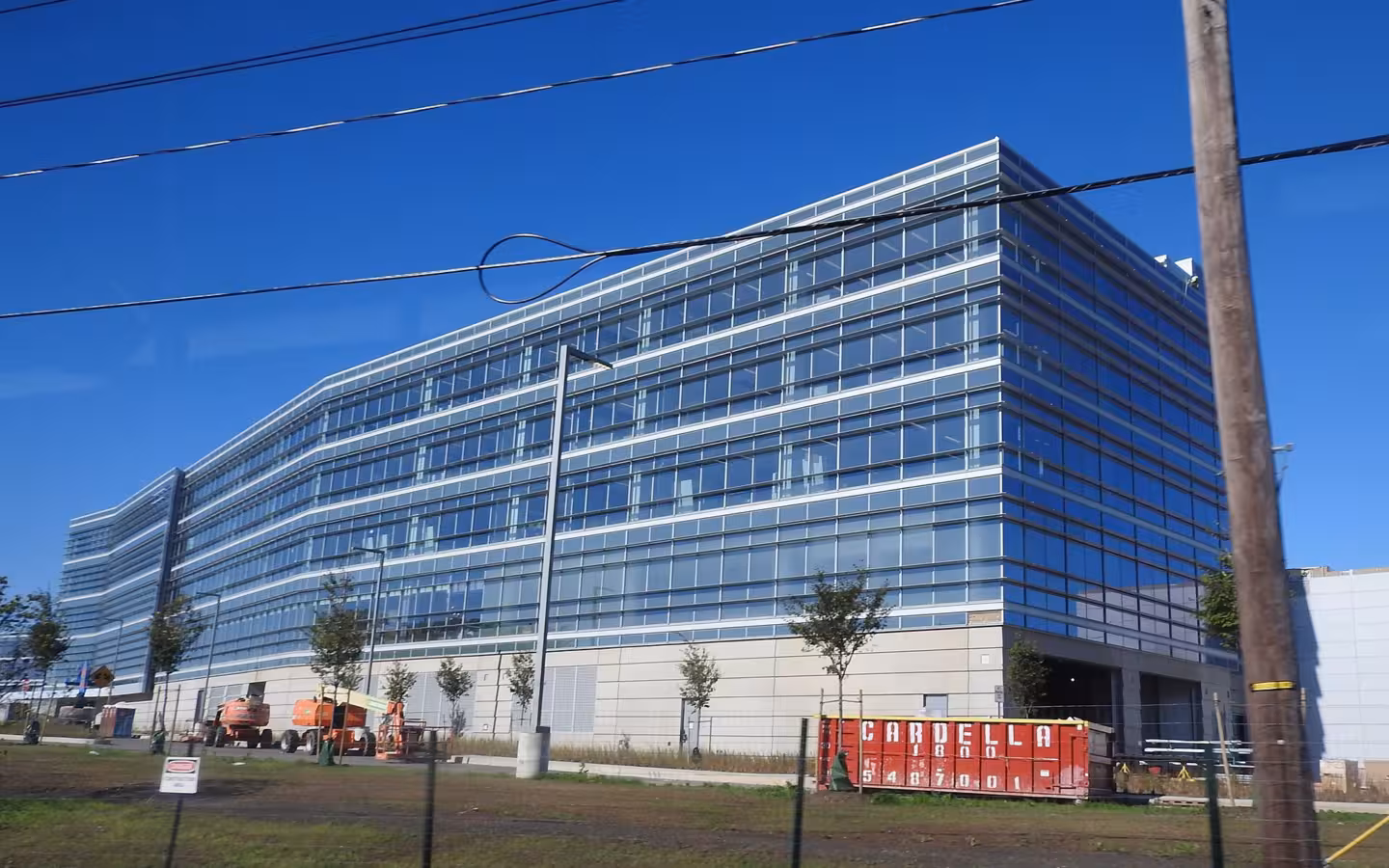 A large modern glass office building under a blue sky with utility wires overhead