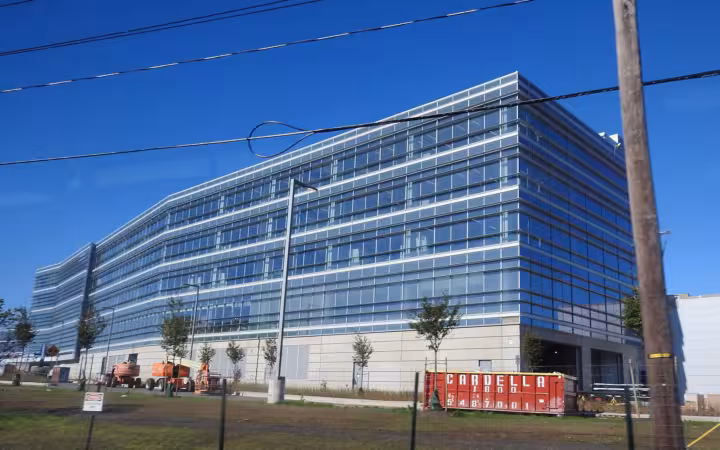 A large modern glass office building under a blue sky with utility wires overhead