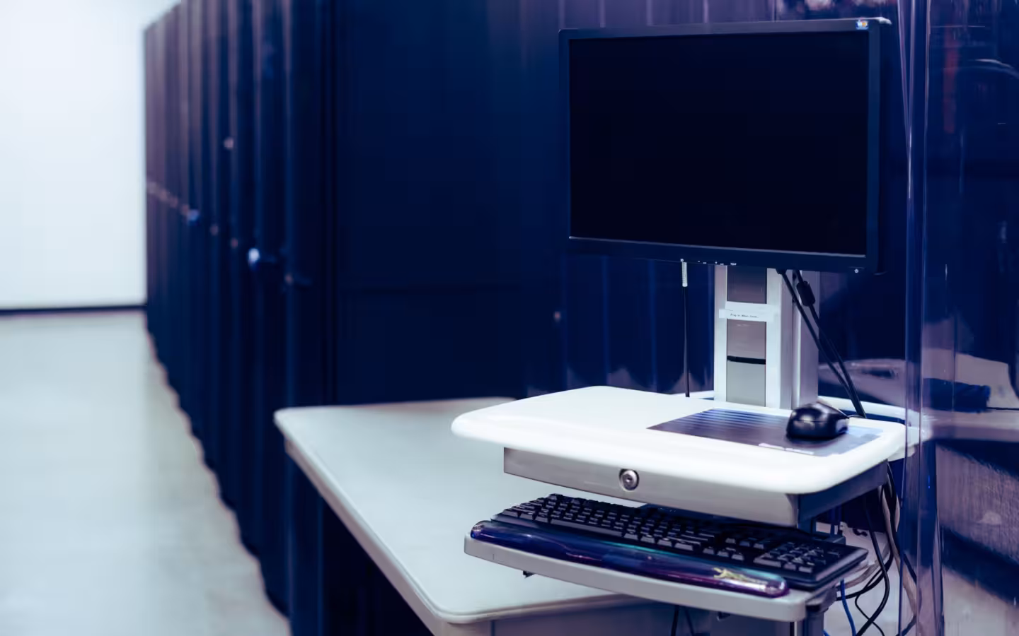 A computer on a stand near a row of server racks in a data center.