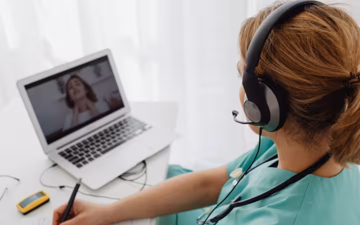 Medical professional wearing a headset consulting a patient online via laptop