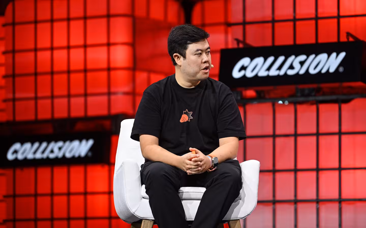 Jesse Lyu sitting on a white chair on a red-lit stage