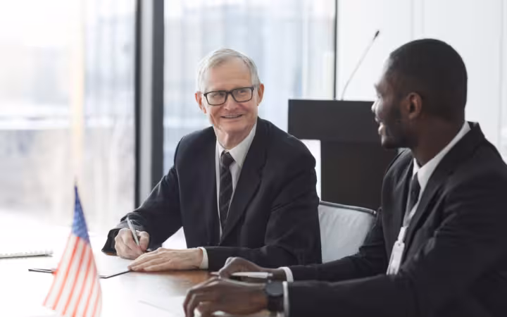 Two business professionals discussing and signing documents at a meeting with an American flag