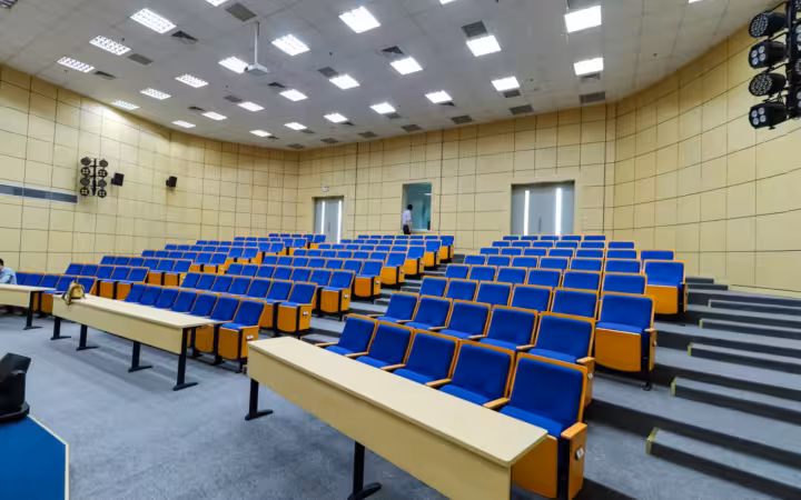 Spacious lecture hall with rows of blue seats and wooden desks