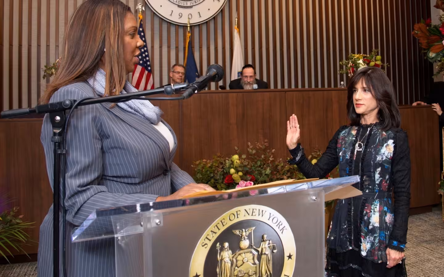 Letitia James speaking at a podium while Rachel Freier raises her hand