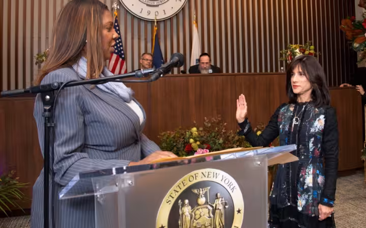 Letitia James speaking at a podium while Rachel Freier raises her hand