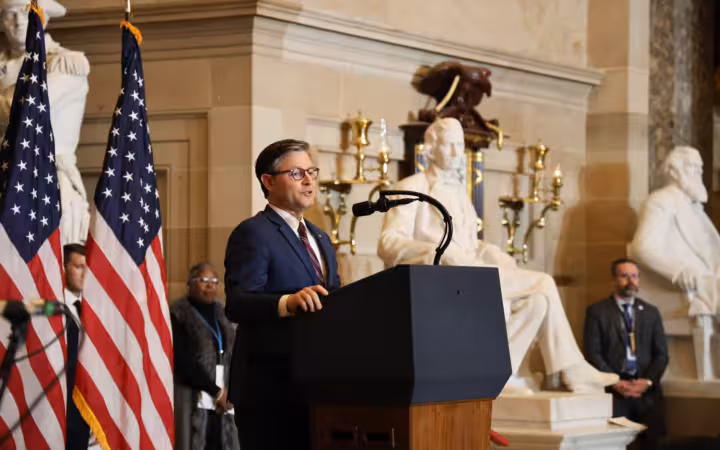 Mike Johnson speaking at a lectern with American flags beside him