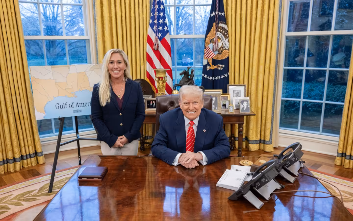 Donald Trump seated at the Oval Office desk with Marjorie Taylor Greene standing.