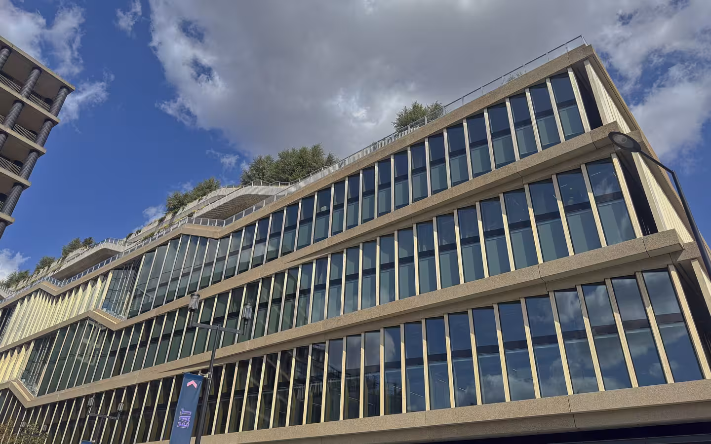 Modern multi‑storey glass‑fronted building with green roof under blue sky