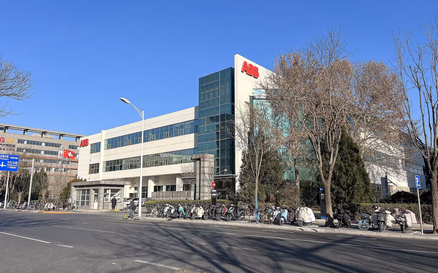 ABB Beijing Drive Systems building across a road, with trees and parked scooters