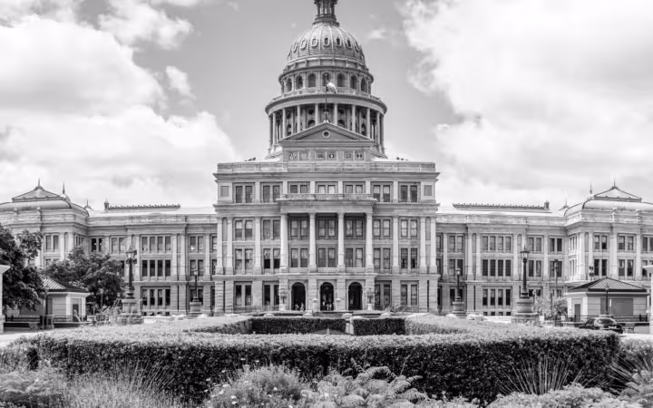 The Texas State Capitol rises behind formal gardens beneath a cloudy sky.