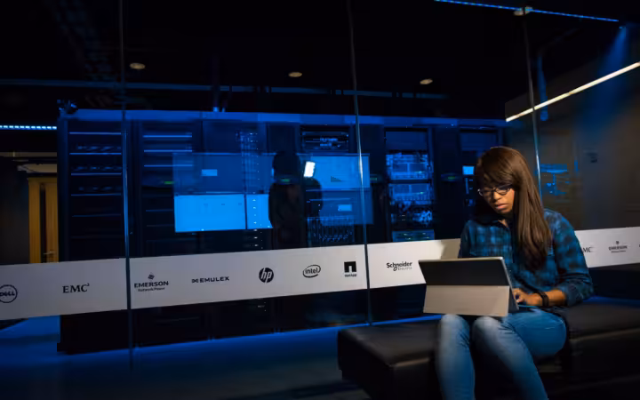 Woman using a laptop in a server room, showcasing modern technology and work environment.