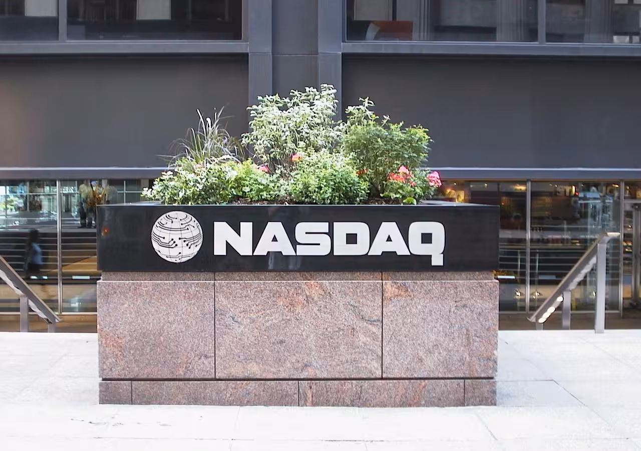 A Nasdaq sign on a stone planter outside a glass-fronted building