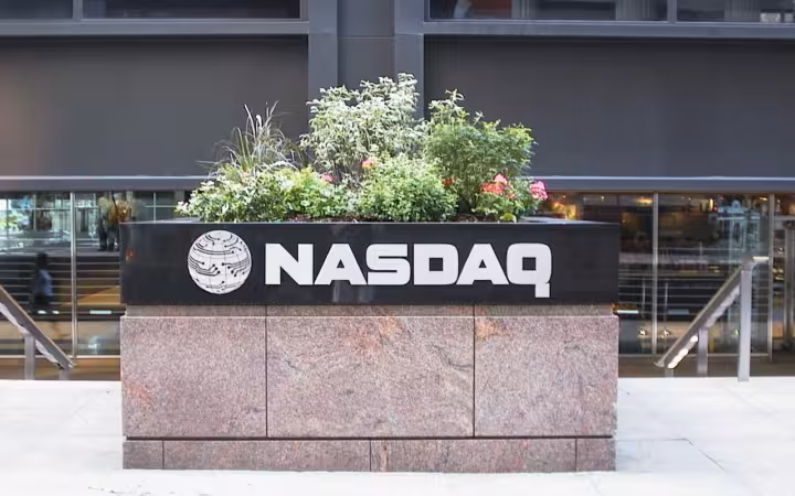A Nasdaq sign on a stone planter outside a glass-fronted building