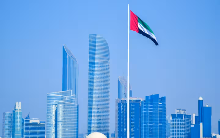 UAE national flag flying above a modern city skyline under blue sky