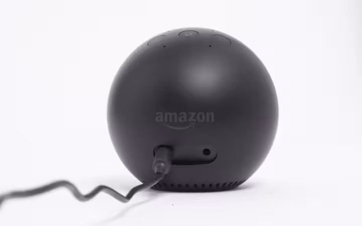 A black spherical Amazon device with a power cord against a white background