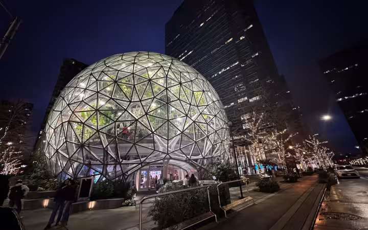 Illuminated Amazon Spheres beside office towers and pedestrians at night