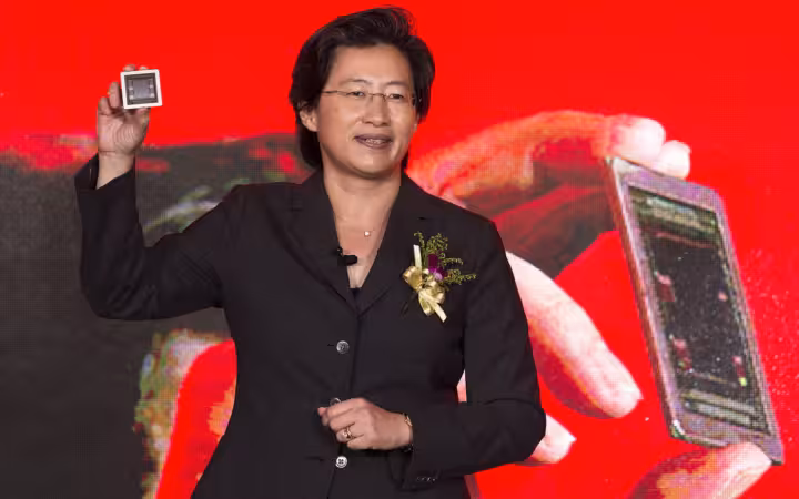AMD CEO Lisa Su holds up a chip before a red presentation screen.