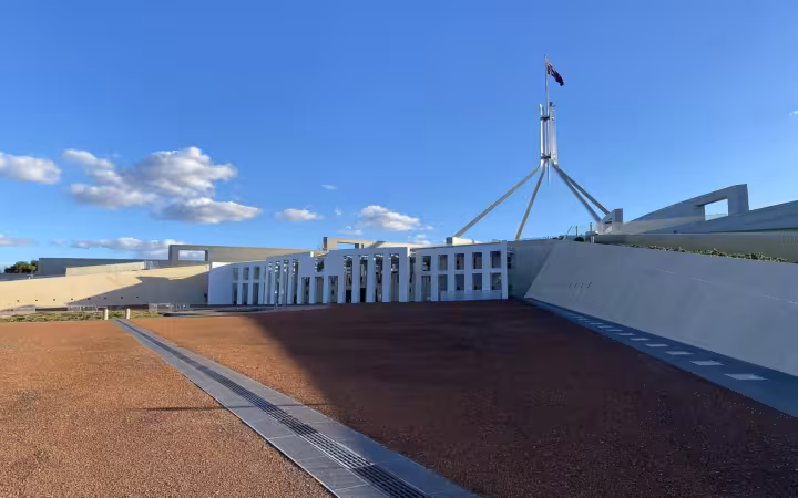 Australian Parliament House beneath a blue sky, across a broad empty forecourt