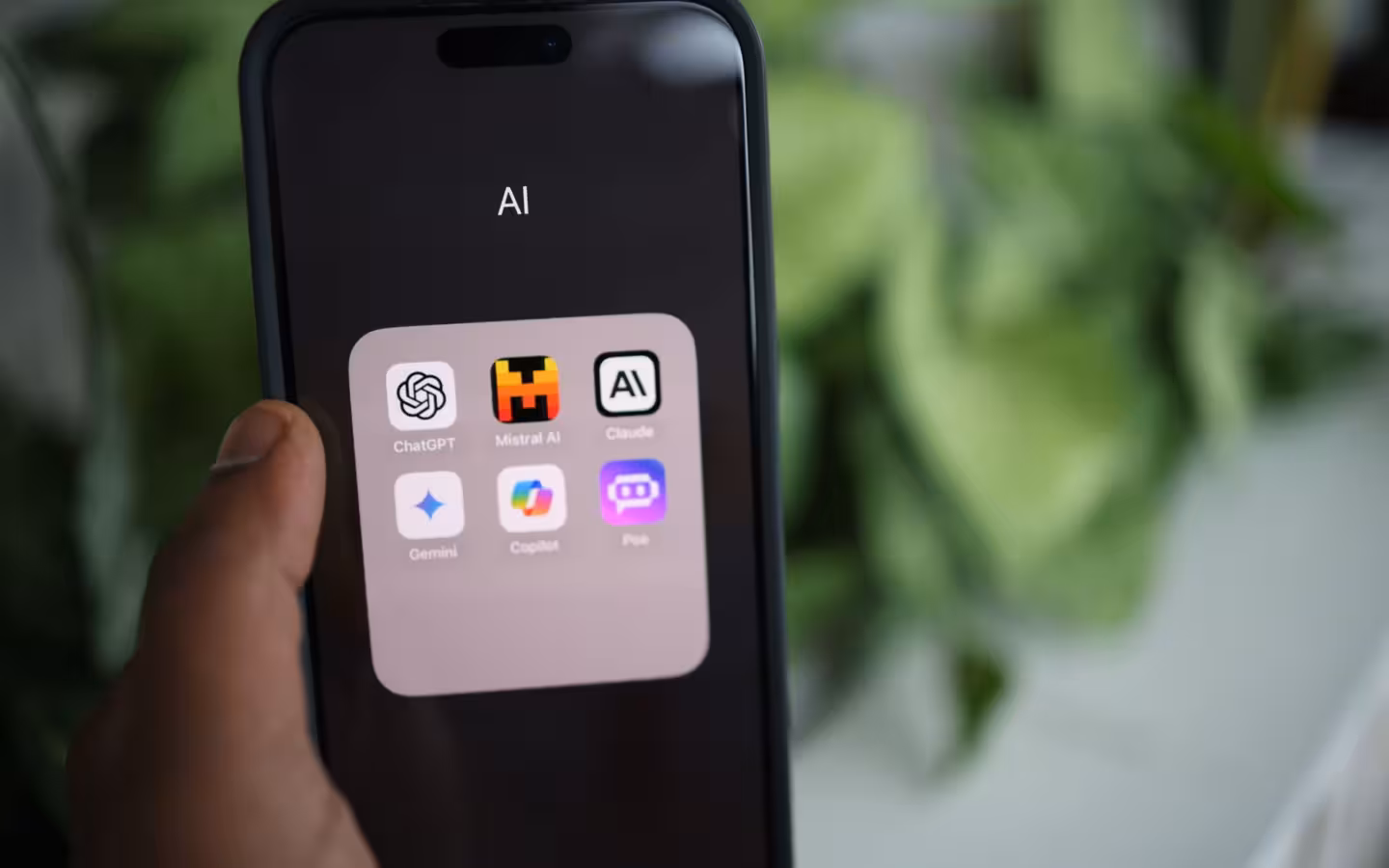 A hand holds a smartphone displaying Claude and several other AI app icons.