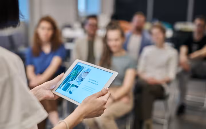 Business seminar with participants focused on a tablet presentation in an office setting.