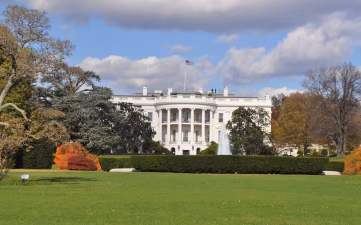 The White House beyond a lawn, hedges, trees and a fountain.