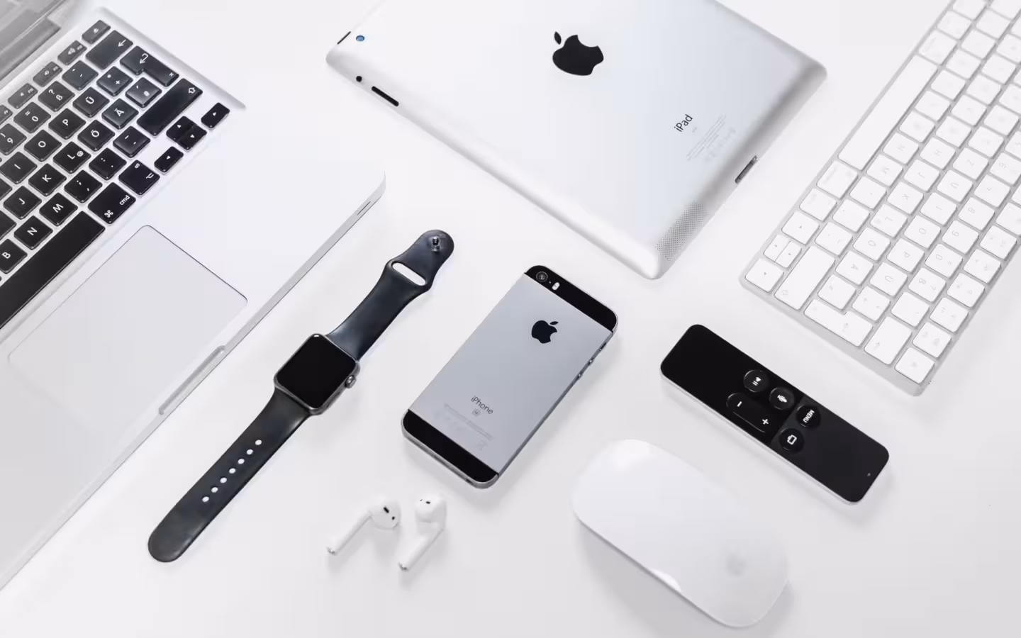 Apple iPhone, iPad, MacBook and Watch arranged with accessories on white.