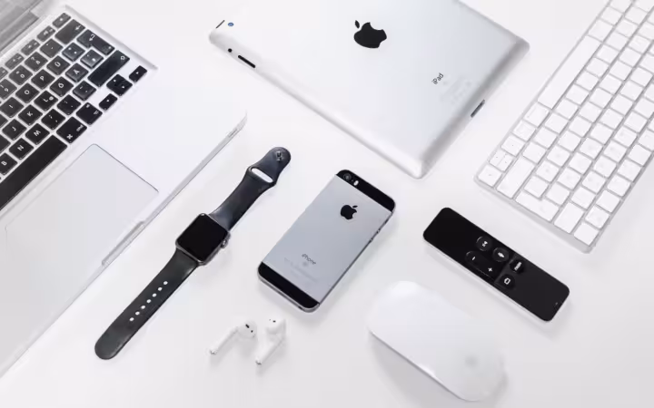 Apple iPhone, iPad, MacBook and Watch arranged with accessories on white.