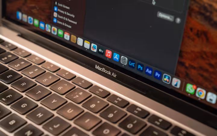 An Apple MacBook Air keyboard and screen with macOS settings and app icons