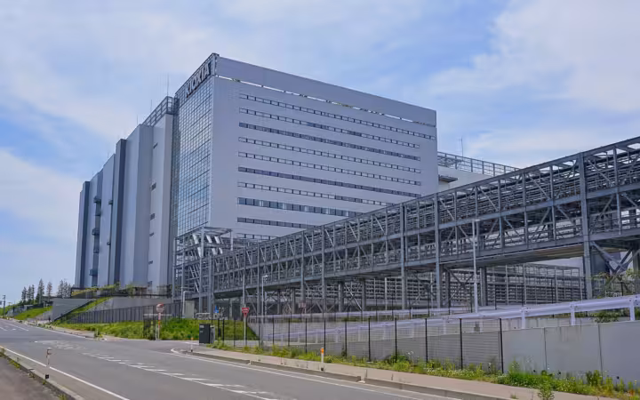 Large modern industrial semiconductor manufacturing plant building with KIOXIA sign under cloudy sky