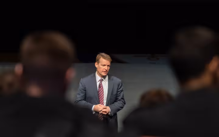 Kevin Mandia speaks at a cyber lecture behind blurred audience members.