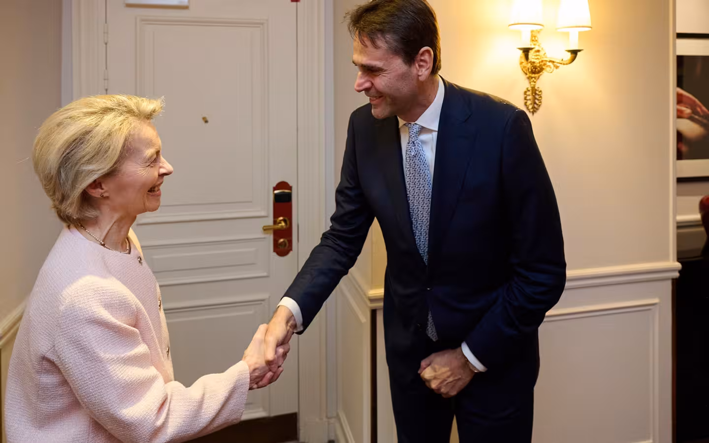 Ursula von der Leyen and Christophe Fouquet smiling and shaking hands indoors.