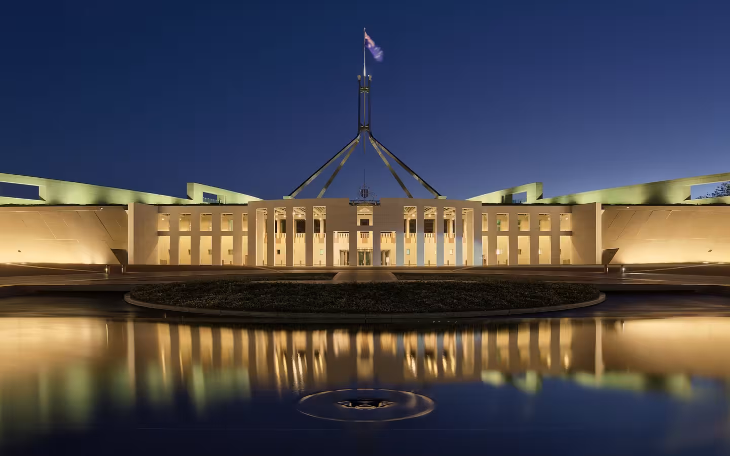Parliament House in Canberra illuminated at dusk and reflected in water