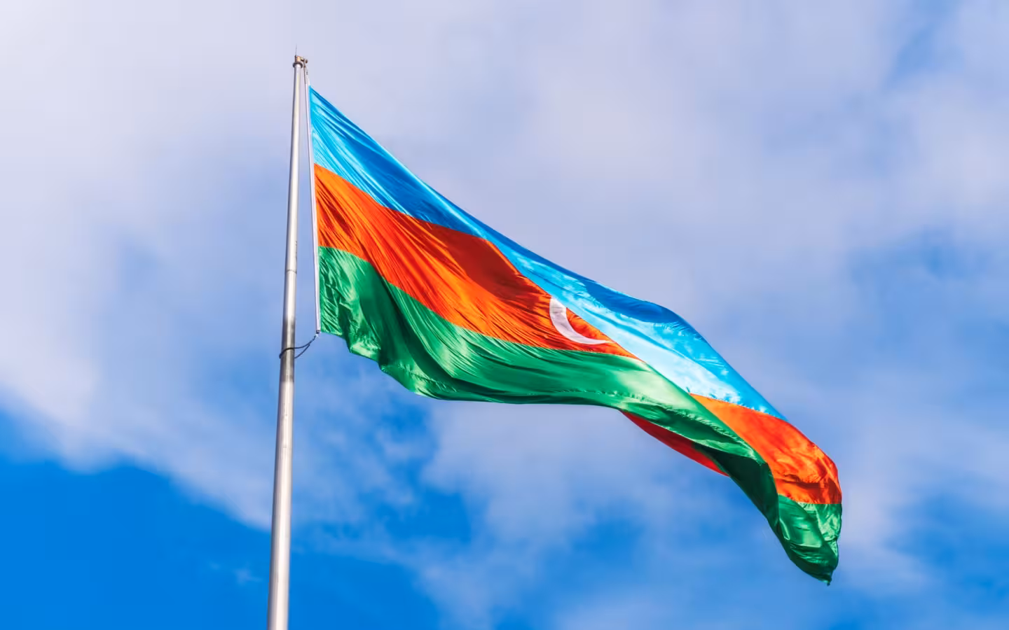 Azerbaijan flag waving from a pole against a partly cloudy sky
