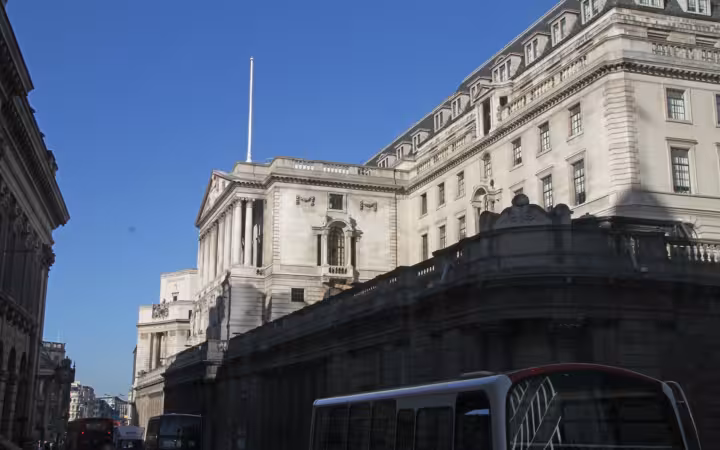 The Bank of England building rises above buses on a London street.