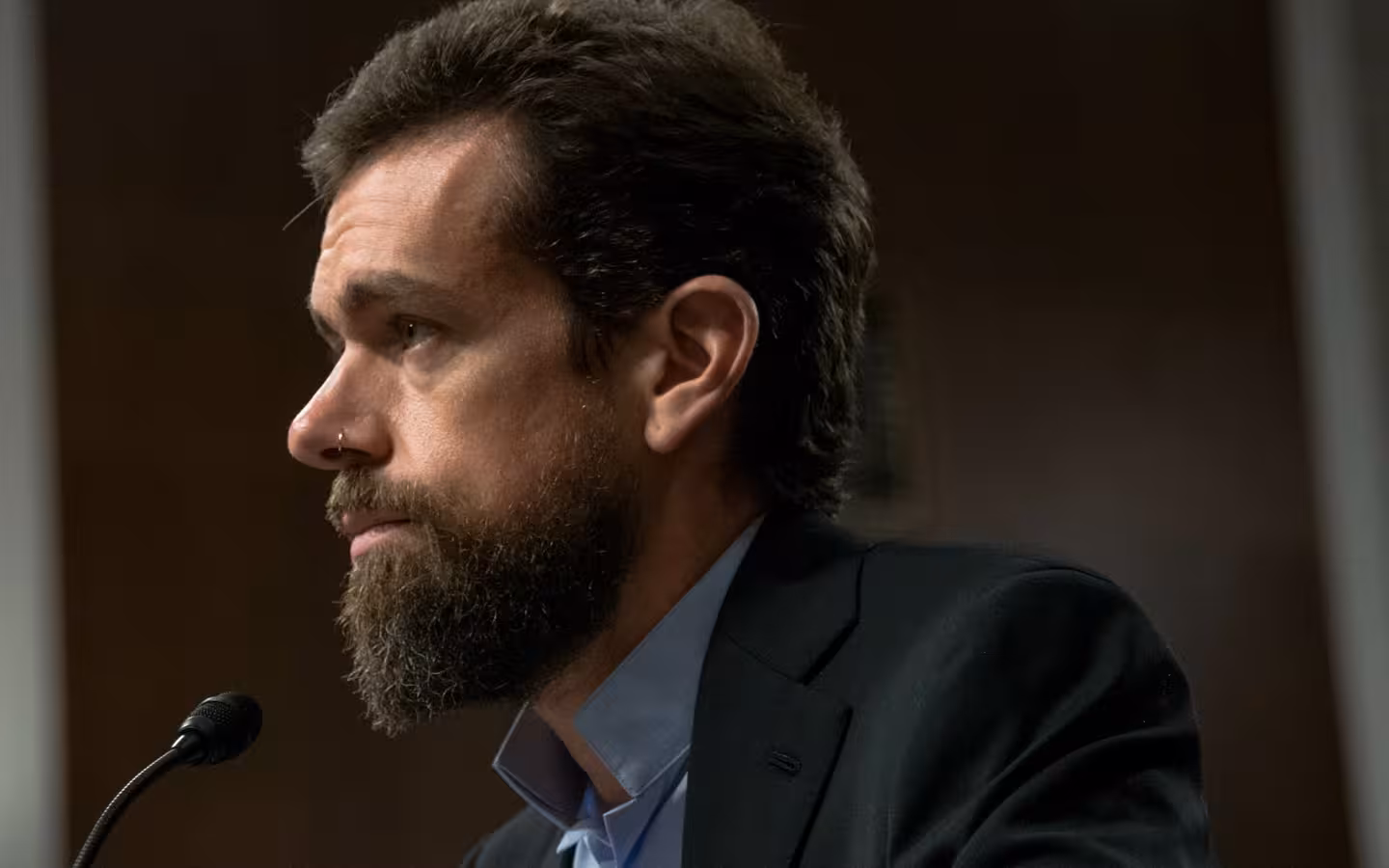 Jack Dorsey in profile beside a microphone against a dark background