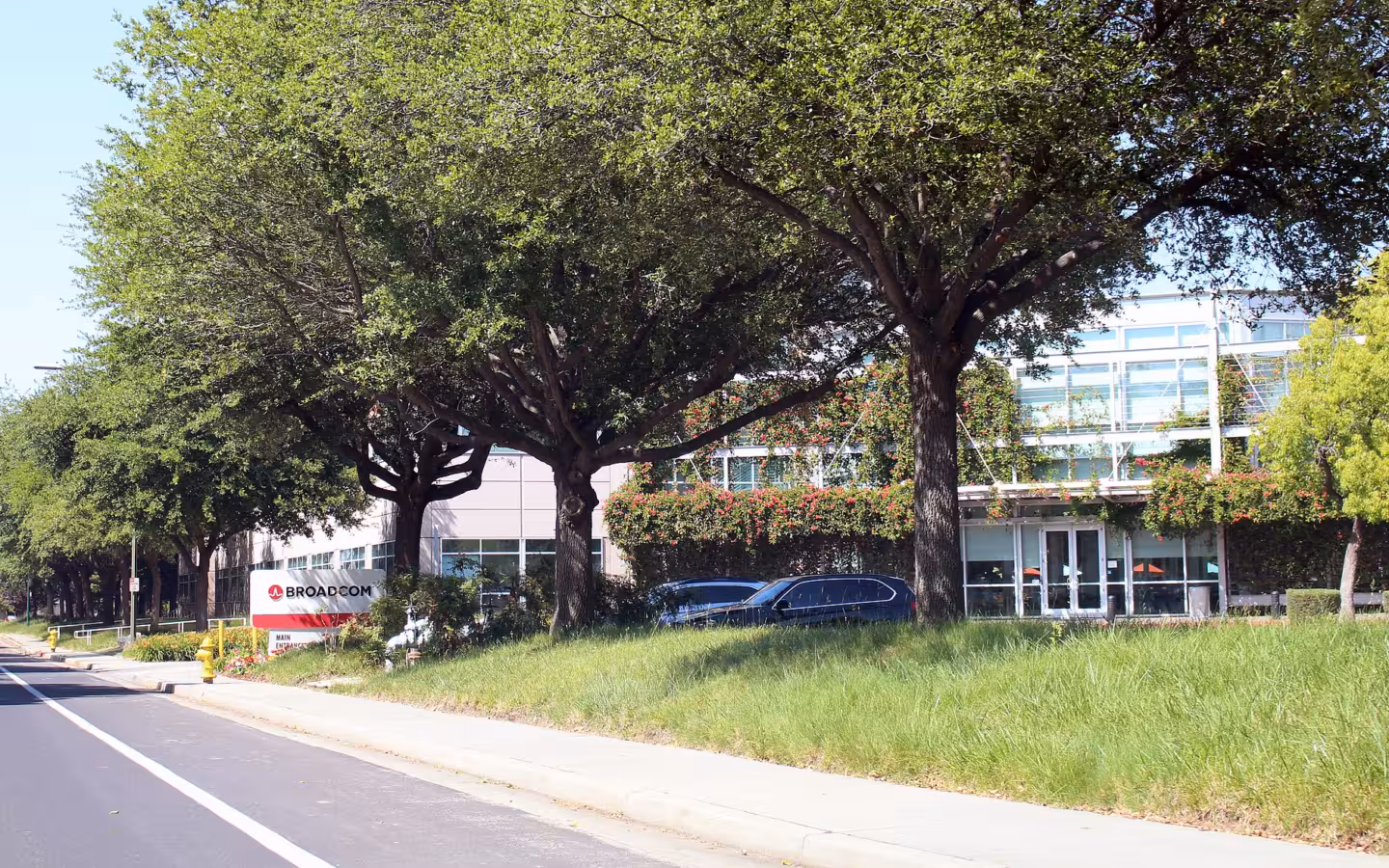 Broadcom headquarters in San Jose behind trees, with a roadside sign