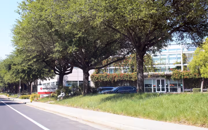 Broadcom headquarters in San Jose behind trees, with a roadside sign