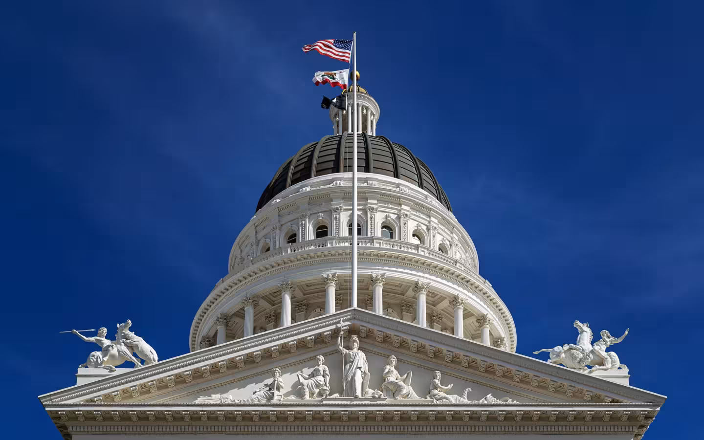 California State Capitol dome, pediment and flags beneath a blue sky