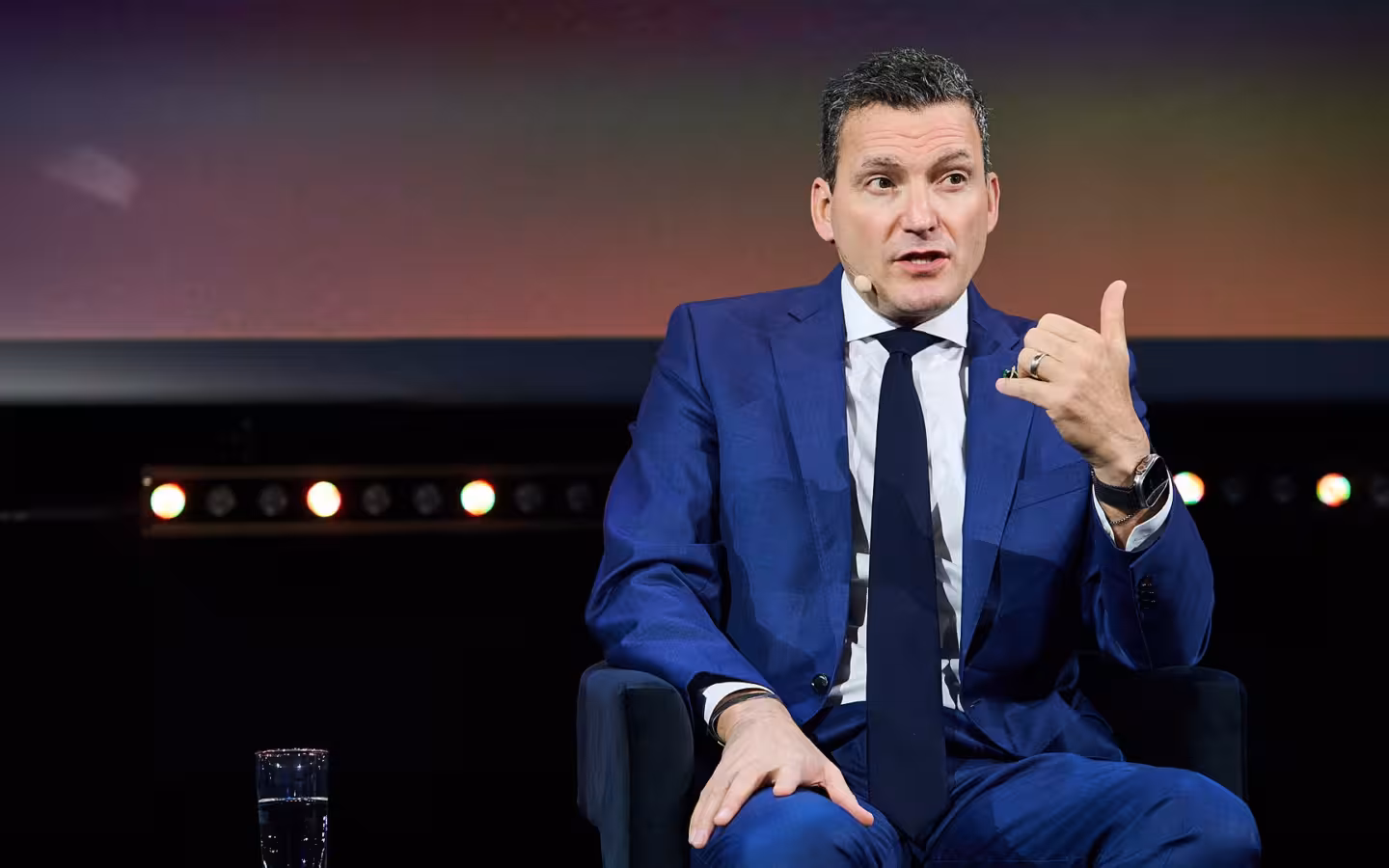 Evan Solomon speaks into a headset microphone while seated onstage.
