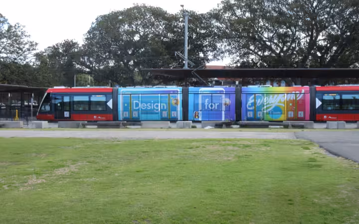 A Sydney tram carries a colourful Canva design advertisement beside a lawn.