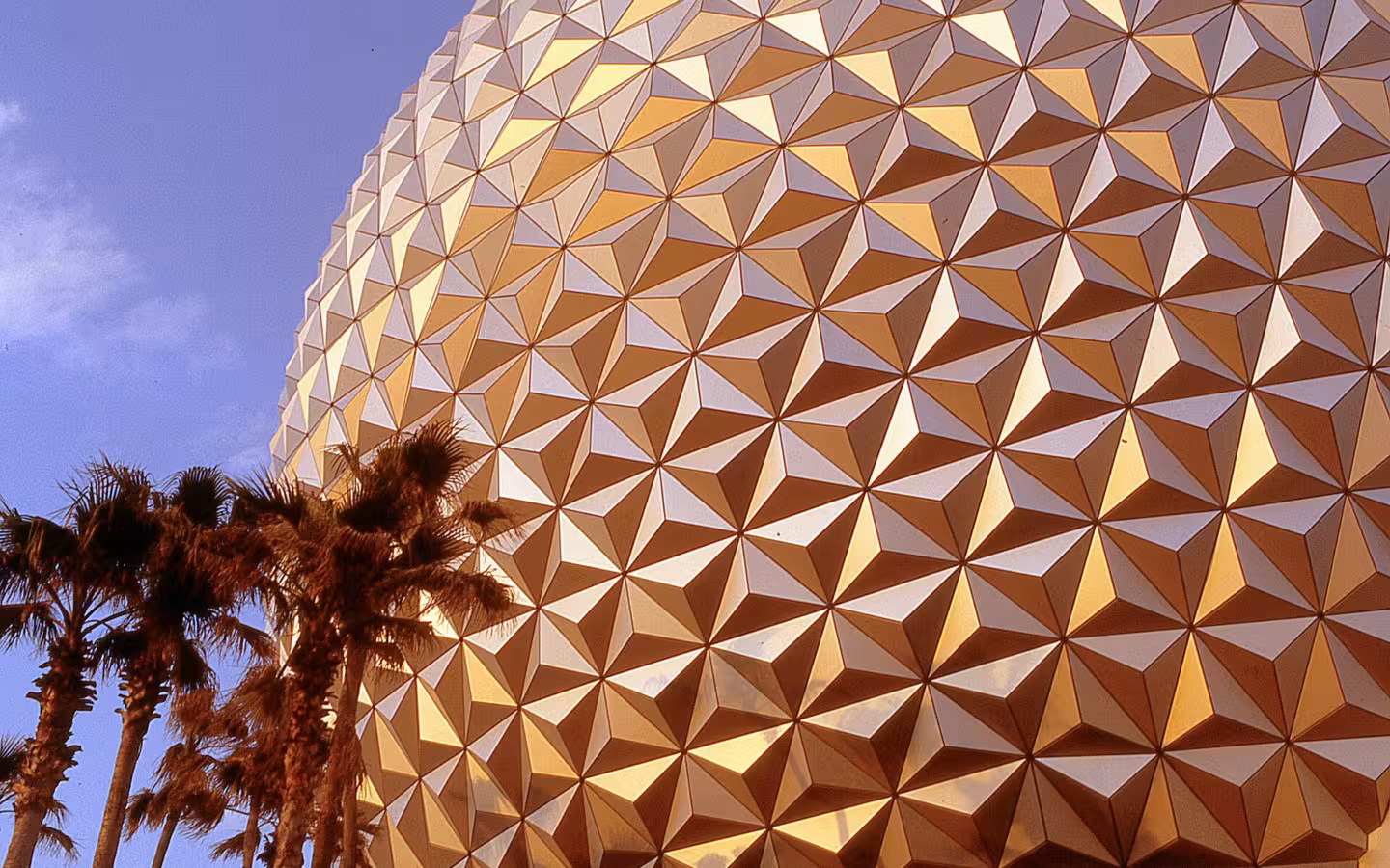 Spaceship Earth dome at Epcot glowing in evening light beside palm trees