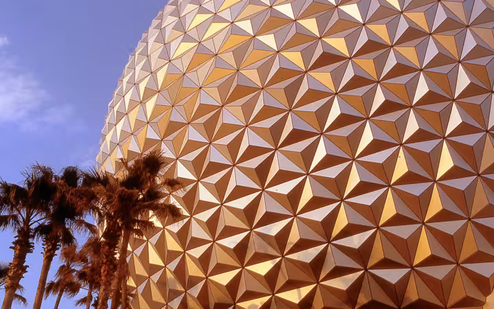 Spaceship Earth dome at Epcot glowing in evening light beside palm trees