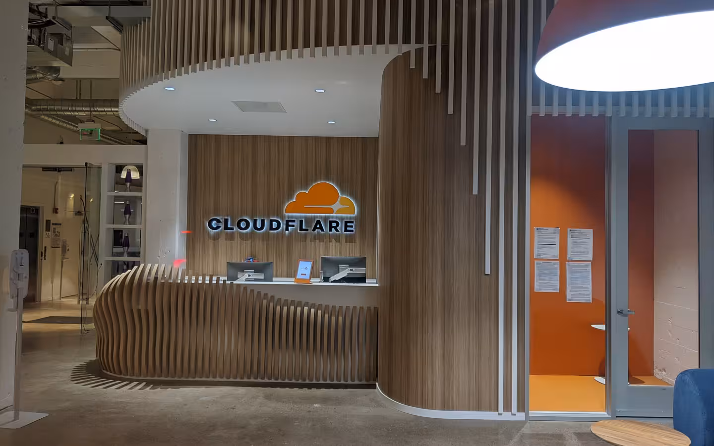 Cloudflare office reception area with an illuminated logo and curved wooden desk