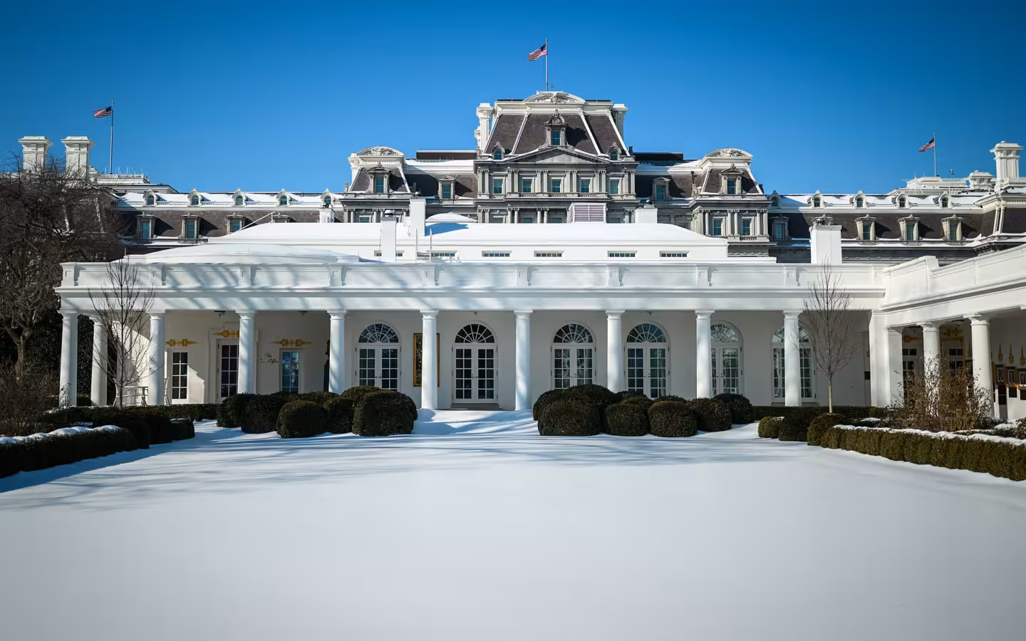 The White House complex behind a snow-covered lawn under blue skies